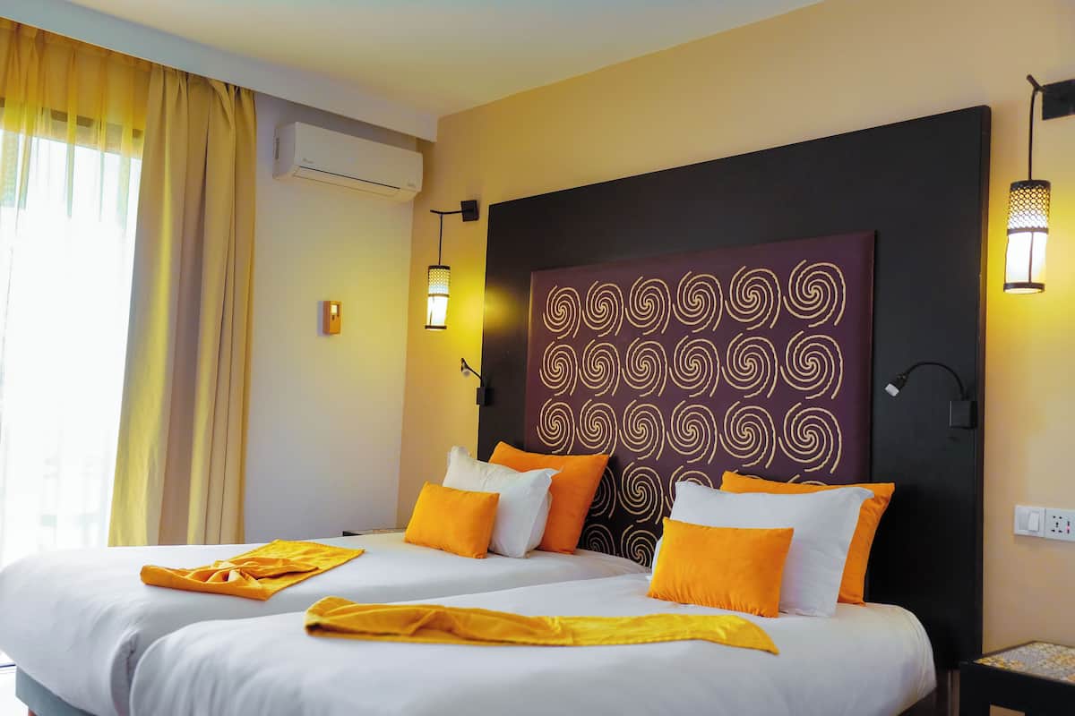 Quarto de hotel com cama, cortinas, ar condicionado fixado na parede, painel decorativo e abajures.