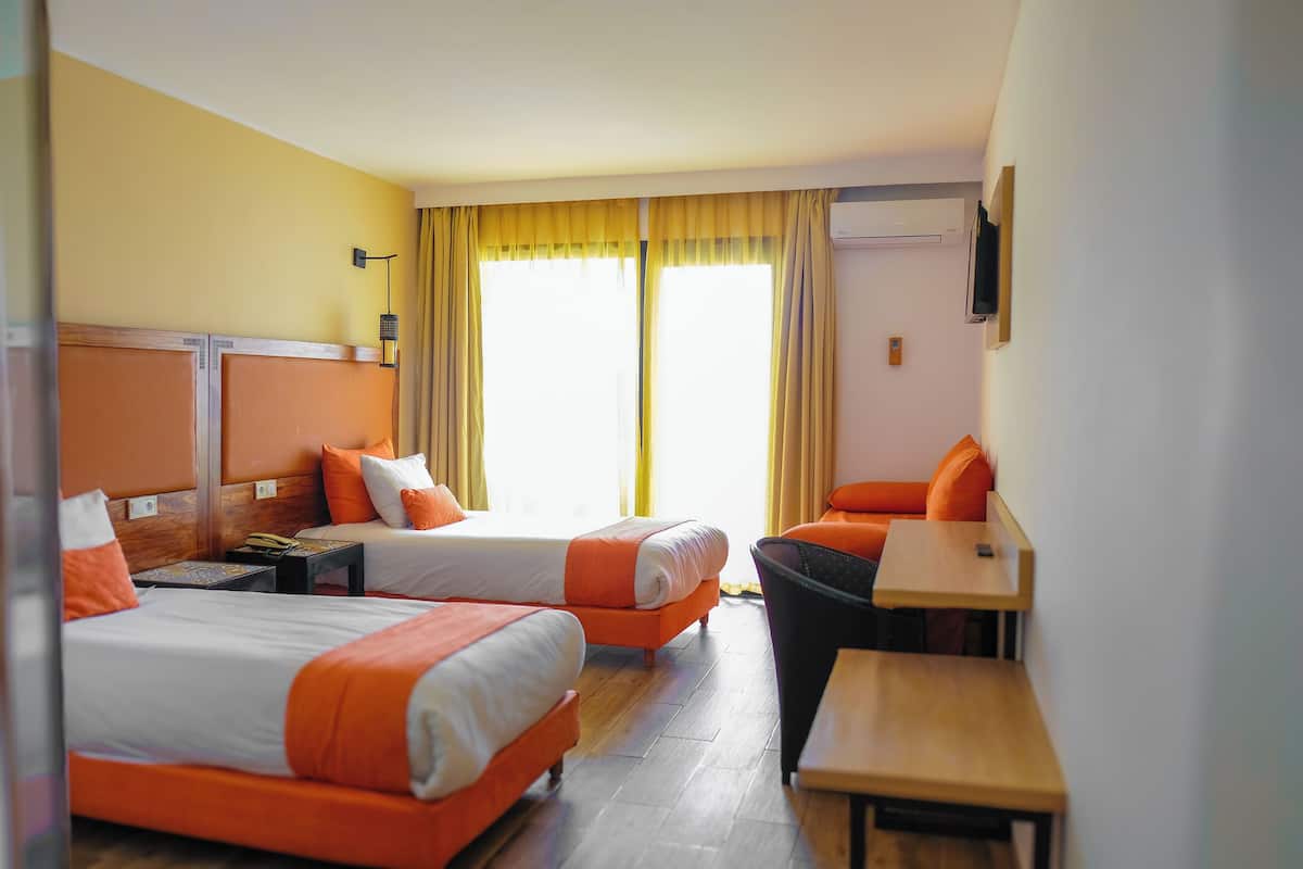 Quarto de hotel com duas camas, uma escrivaninha, uma cadeira e uma televisão.