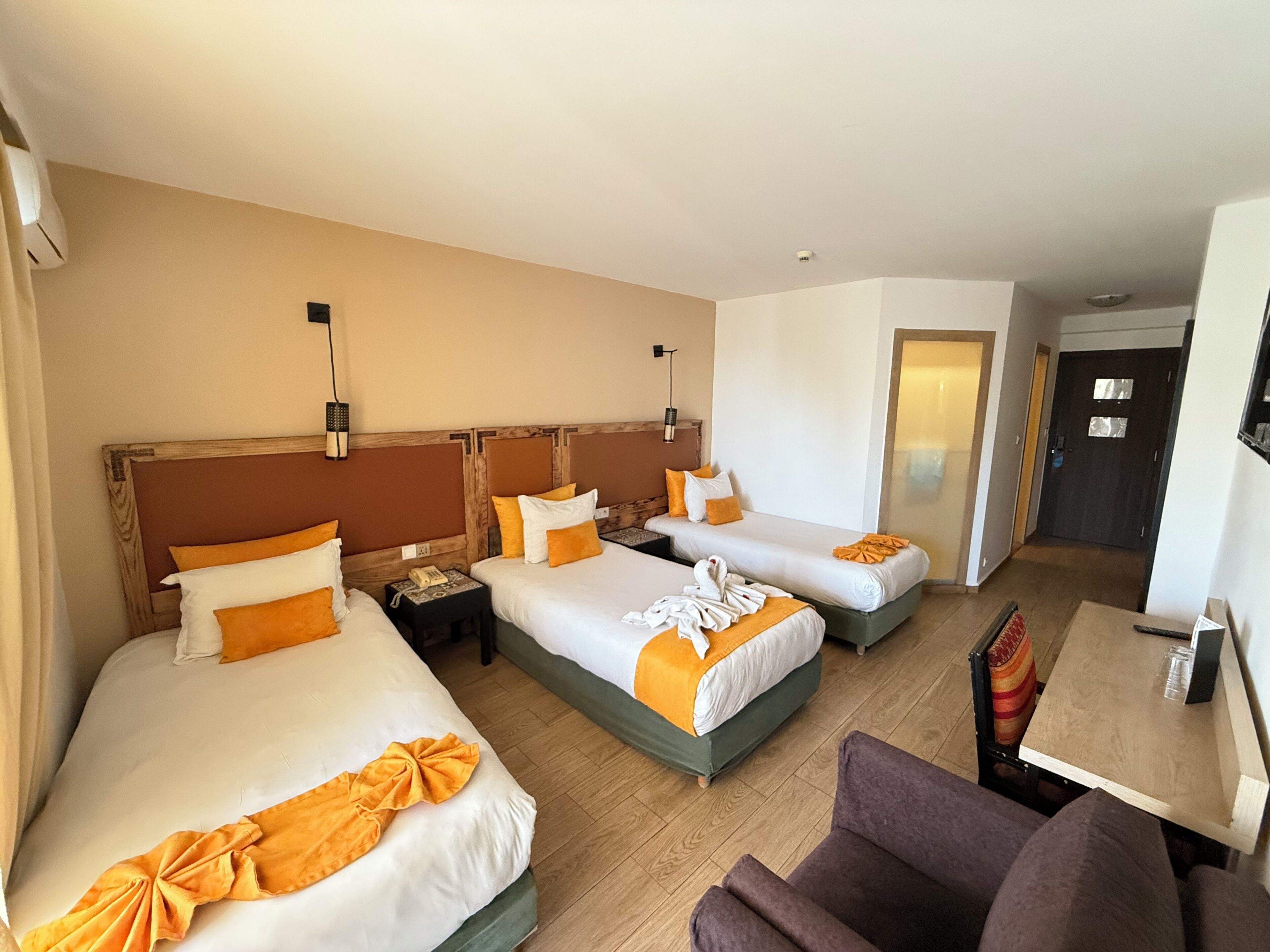 A hotel room with three beds, a small table, a chair, and a door.