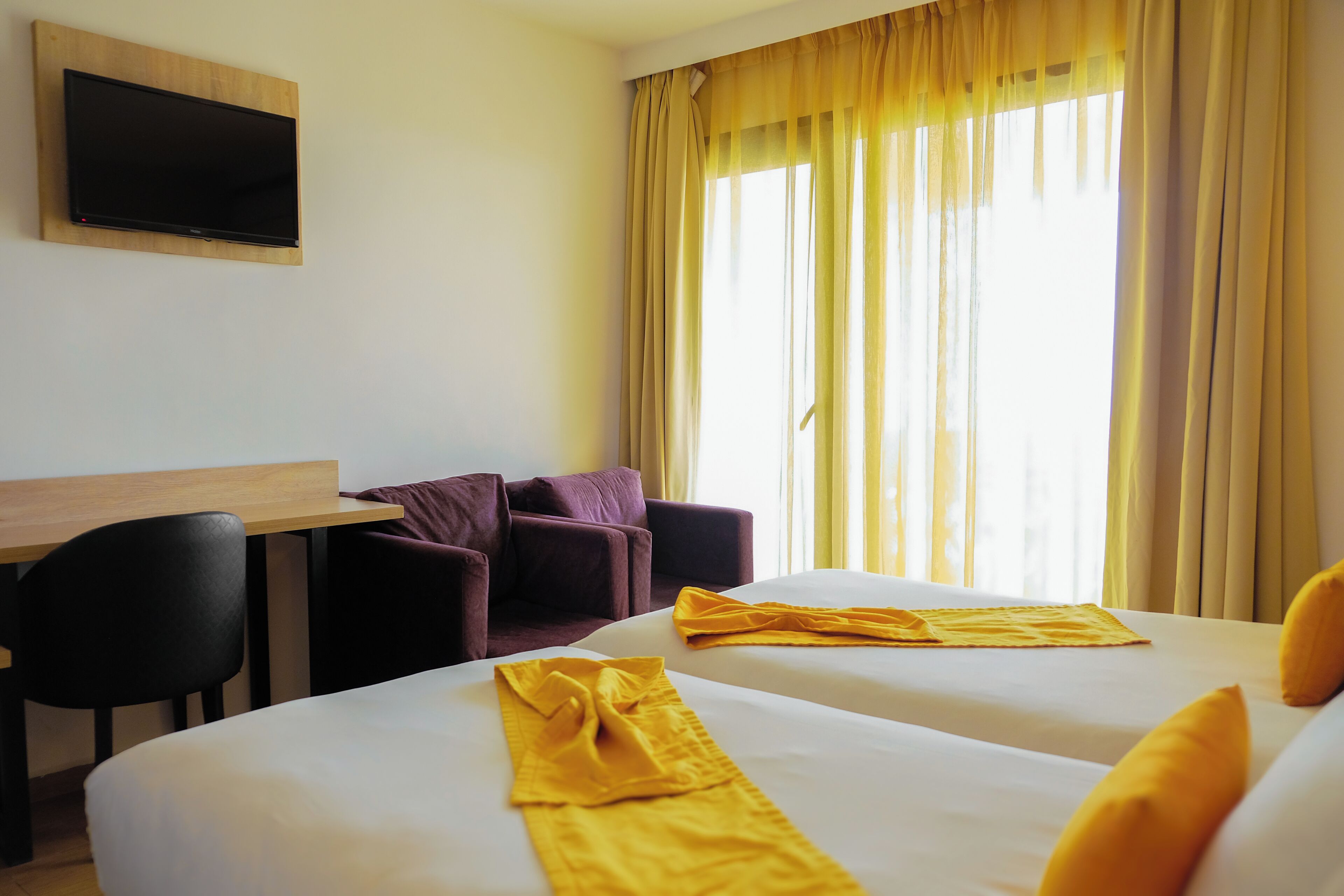 Ein Hotelzimmer mit zwei Betten, einem Schreibtisch, einem Sessel und einem an der Wand befestigten Fernseher.