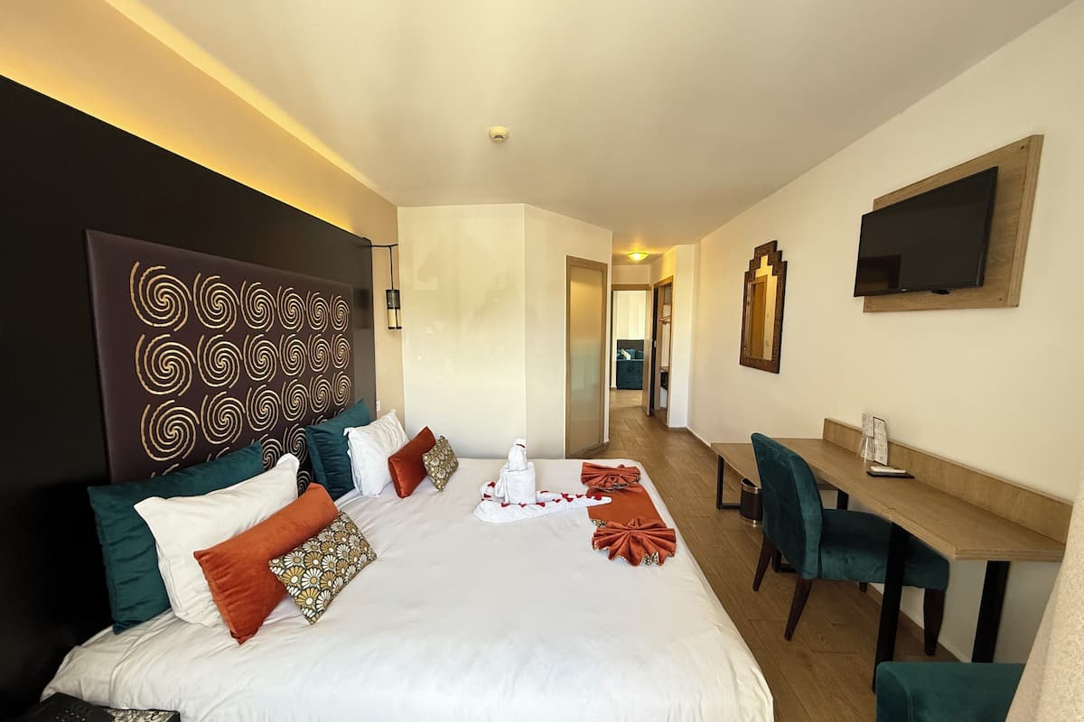 Quarto de hotel com uma cama grande, uma mesa, uma cadeira, uma televisão e um espelho.