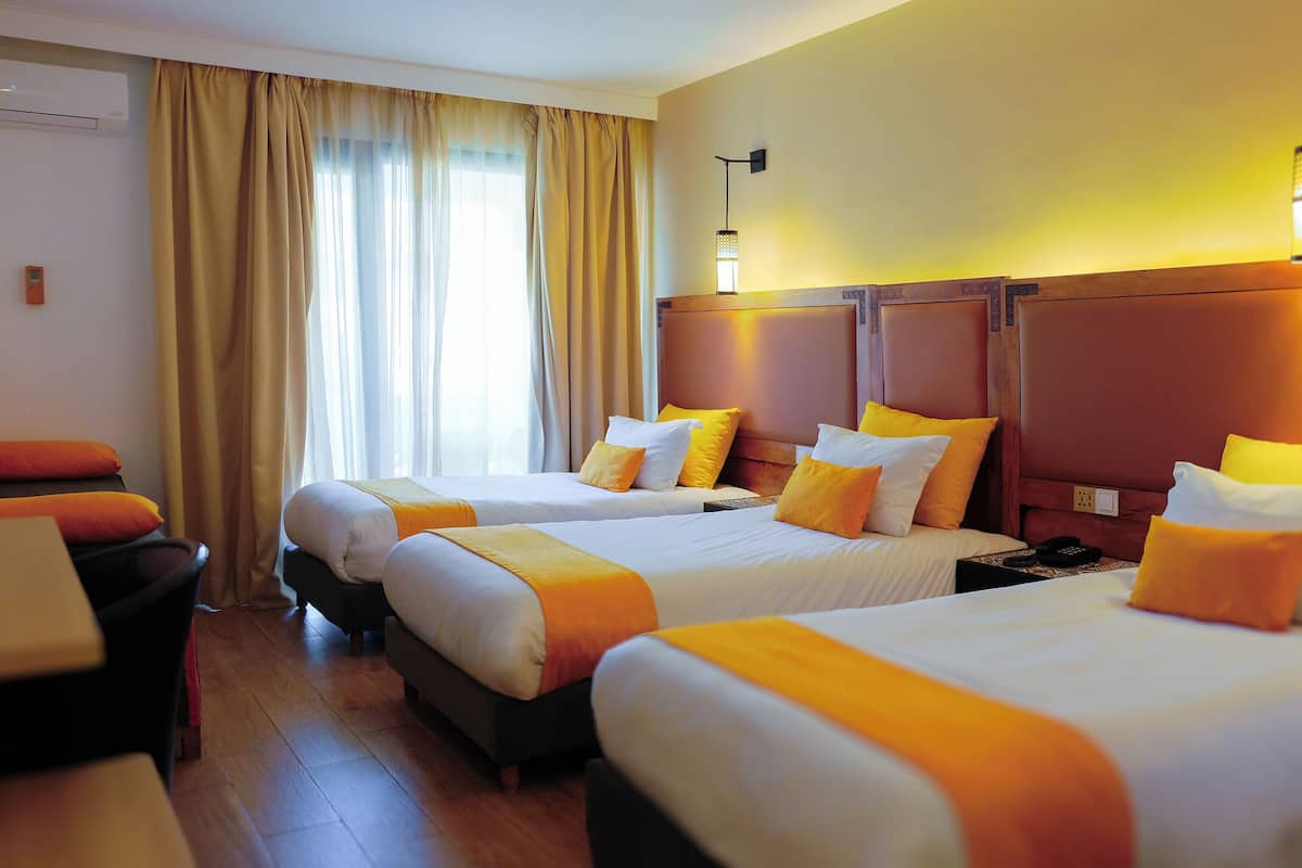 Quarto de hotel com três camas, uma escrivaninha e uma cadeira.