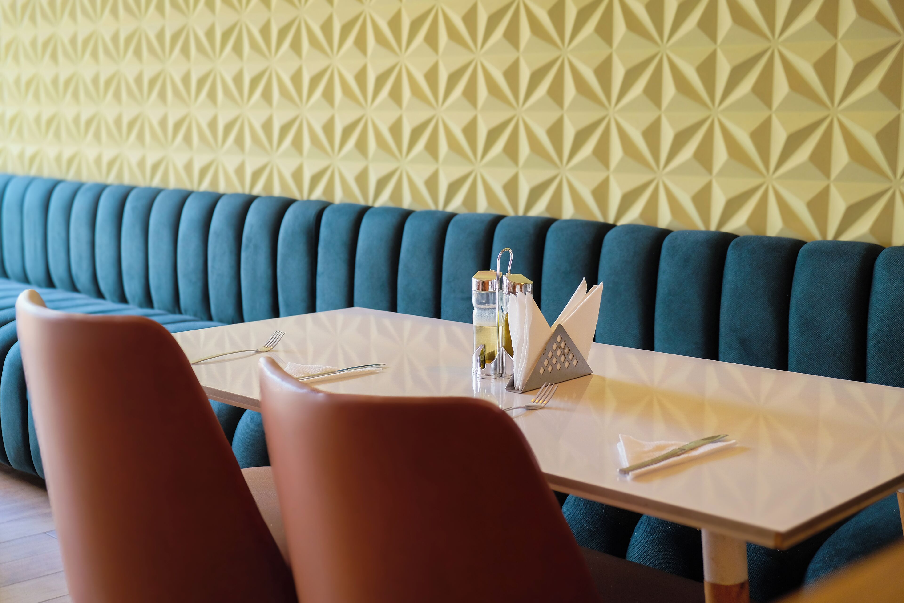 A restaurant with a teal upholstered bench, a white table, and red chairs.