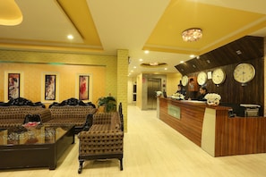 A hotel lobby with a reception desk, multiple clocks, a sofa, and a coffee table. - Hotel Castle Blue (New Delhi)