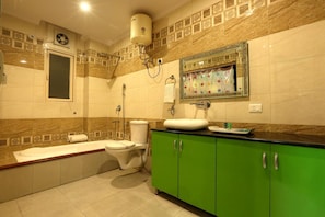A bathroom with a bathtub, toilet, green cabinets, a mirror with a floral design, and a ceiling fan. - Hotel Castle Blue (New Delhi)