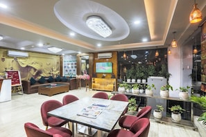 A hotel lobby with a reception desk, seating area, television, and potted plants. - Hotel Castle Blue (New Delhi)