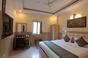 A hotel room with a bed, a desk, a chair, a television, a wardrobe, and a ceiling fan. - Hotel Castle Blue (New Delhi)