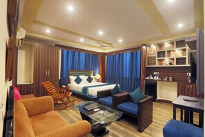 A hotel room with a bed, a seating area with chairs and a table, a kitchenette, and a TV. - Hotel Castle Blue (New Delhi)