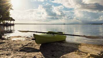 Een kajak op een zandstrand, met kalm water en een boot in de verte.