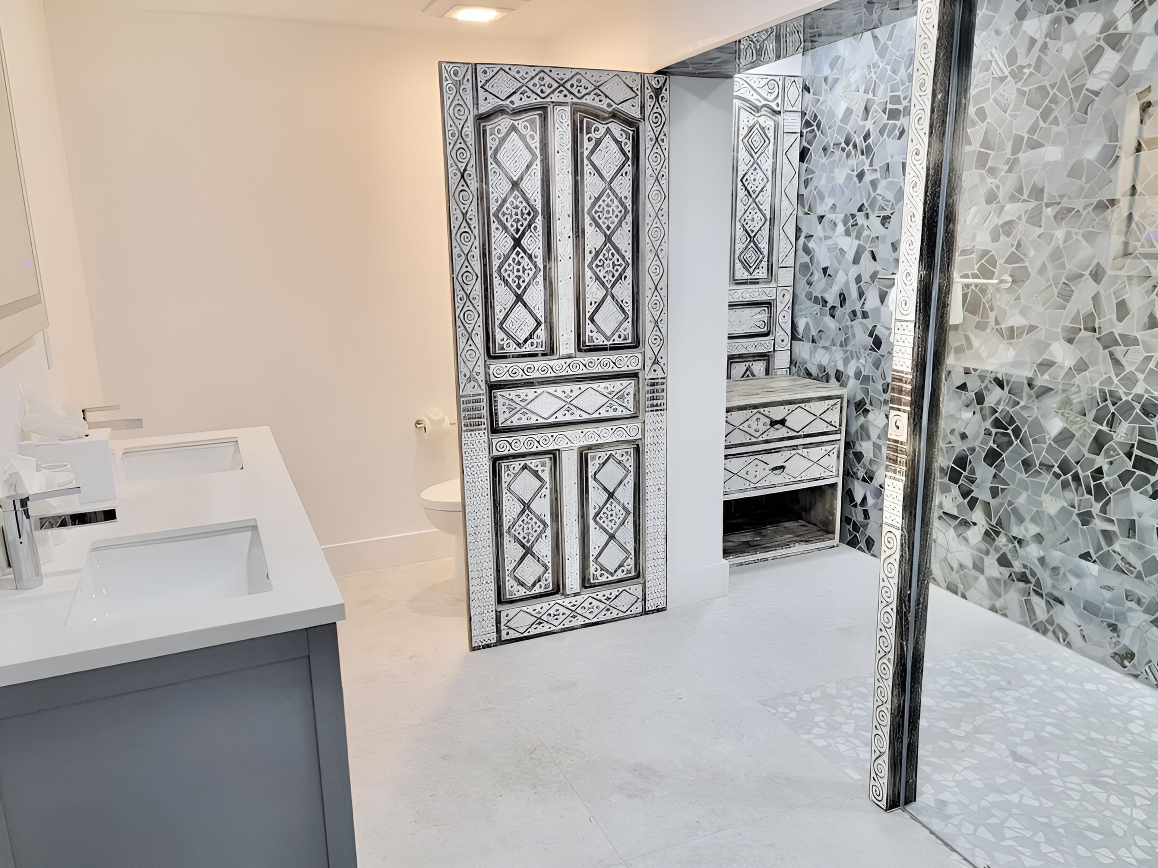 Une salle de bain moderne avec un lavabo blanc, un miroir et un mur décoratif orné de motifs géométriques.