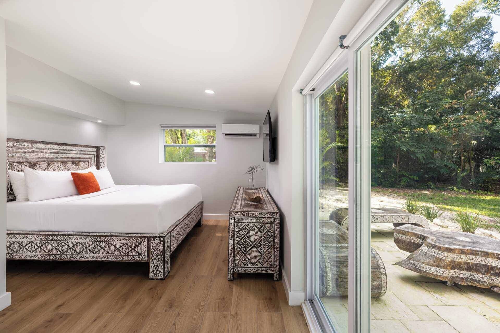 A bedroom with a large bed, a small bedside table, a TV, and a window overlooking a garden.
