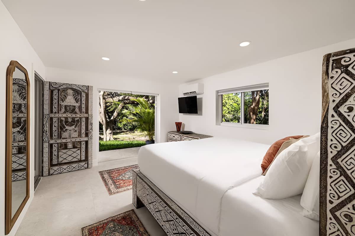 A bedroom with a large bed, a TV, and a window with a view of greenery.
