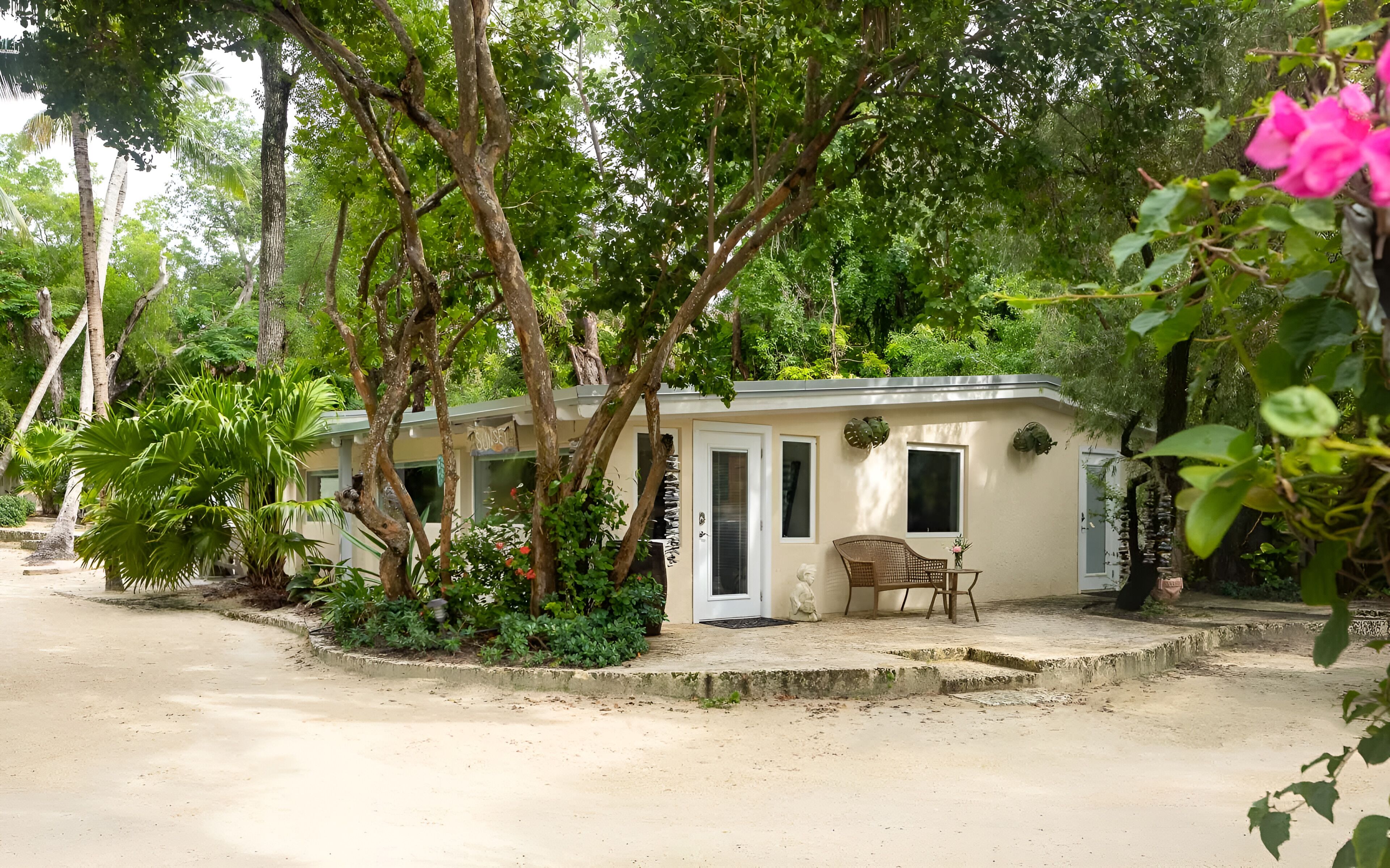 A small, single-story building with a beige exterior, surrounded by lush greenery and trees.