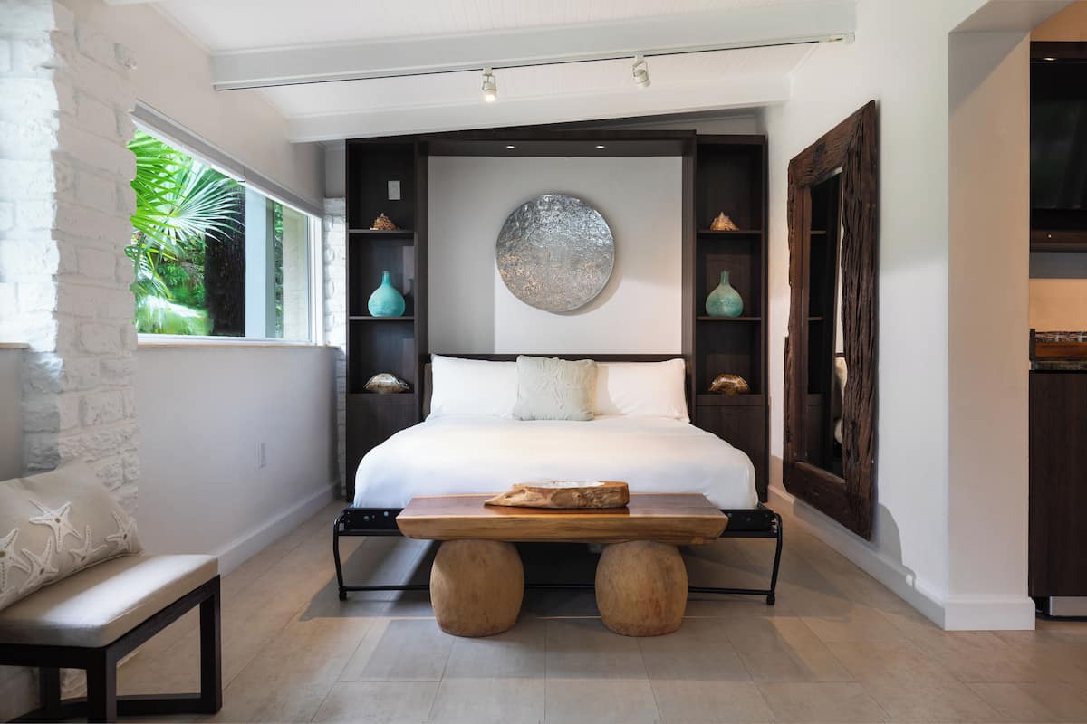 A bedroom with a large bed, a wooden bench, and a decorative wall piece.