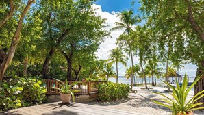 A wooden deck with potted plants, a wooden fence, and a view of the beach and ocean. - Largo Resort (Key Largo)