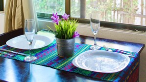 A dining table set with plates, cutlery, and a glass of water, with a potted plant and a window view of greenery. - Casa Frida Holbox (Isla Holbox)