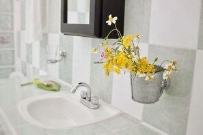 A bathroom with a white sink, a faucet, and a wall-mounted flower pot with yellow and white flowers.