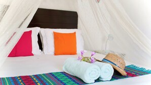 A cozy bed with a canopy, a colorful woven mat, and a rolled white towel. - Casa Frida Holbox (Isla Holbox)