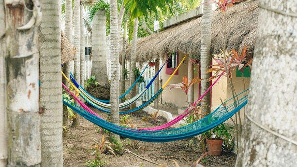 A thatched-roof hut with colorful hammocks strung between trees. - Casa Frida Holbox (Isla Holbox)