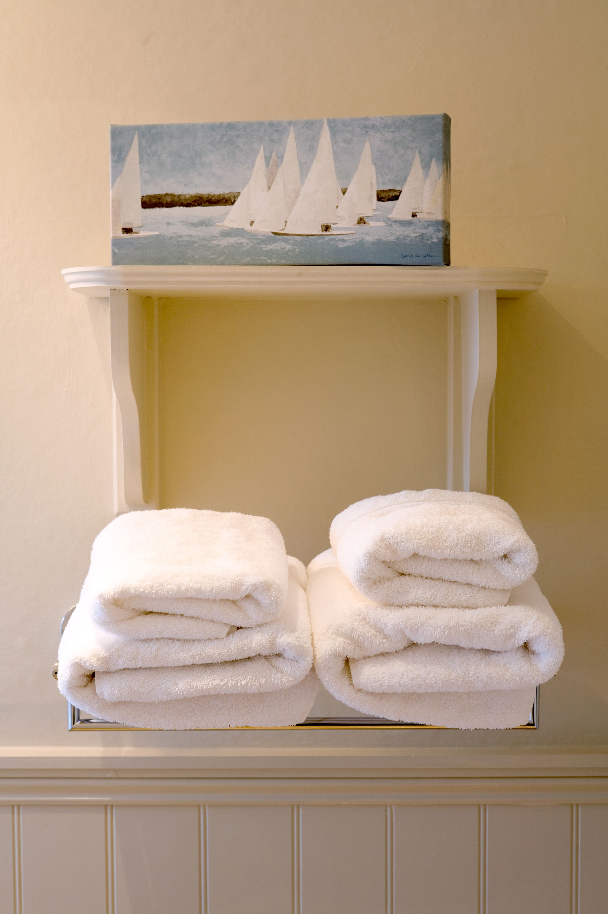 A white shelf with a painting of sailboats and a stack of folded white towels.