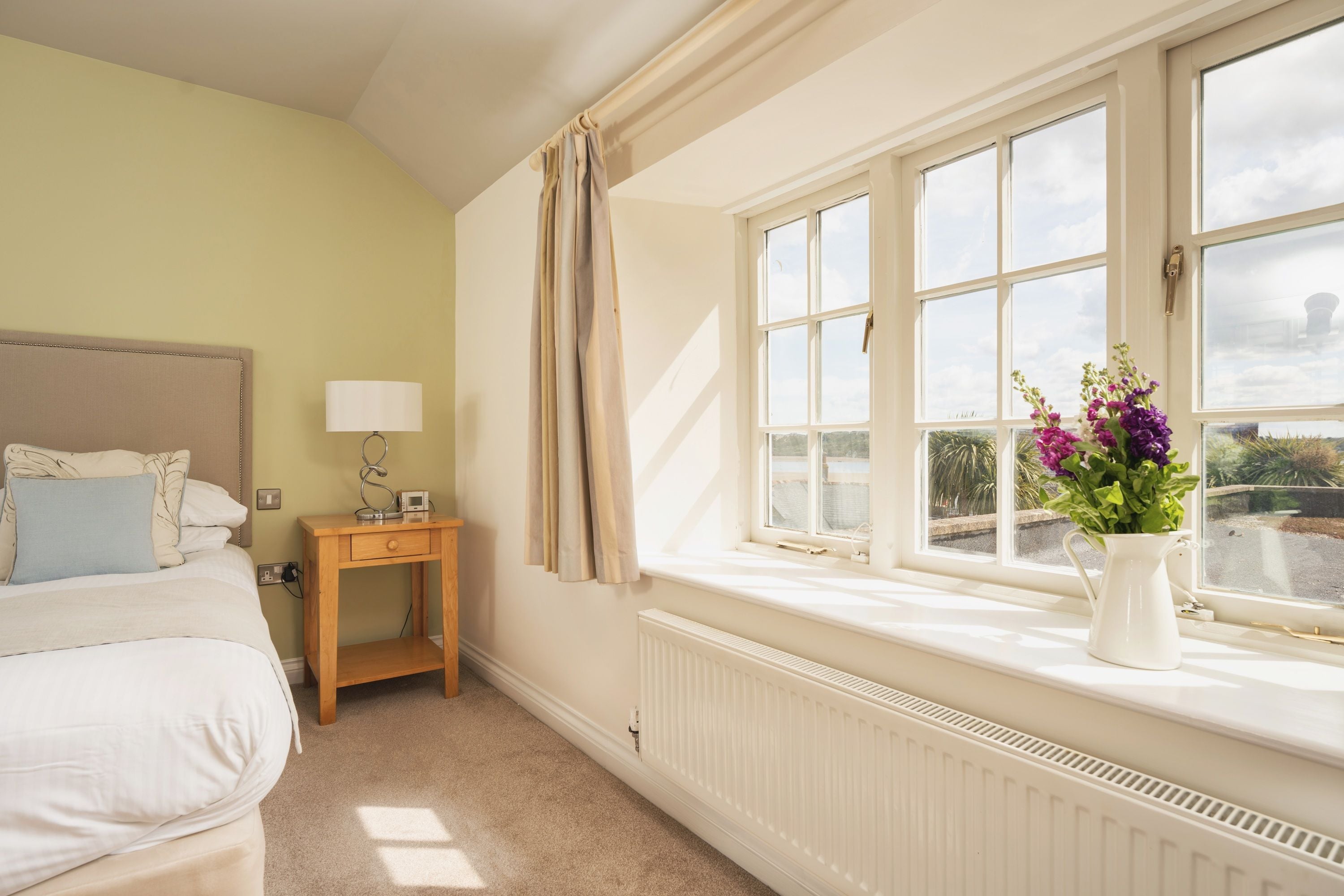 A bedroom with a bed, bedside table, lamp, and a window with a view of the outside.