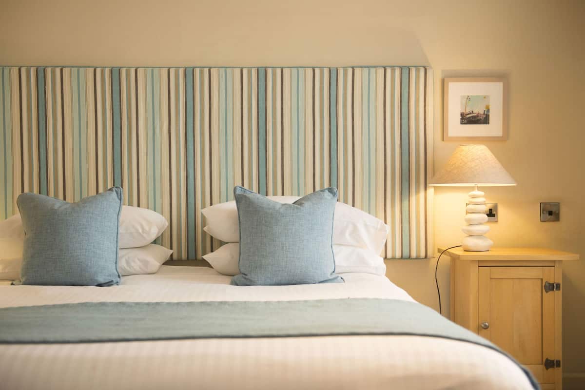 A neatly made bed with two pillows, a striped headboard, a bedside lamp, and a small wooden cabinet.
