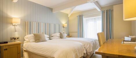 Una habitación de hotel con dos camas, una mesita de noche de madera, un escritorio y una ventana con cortinas.