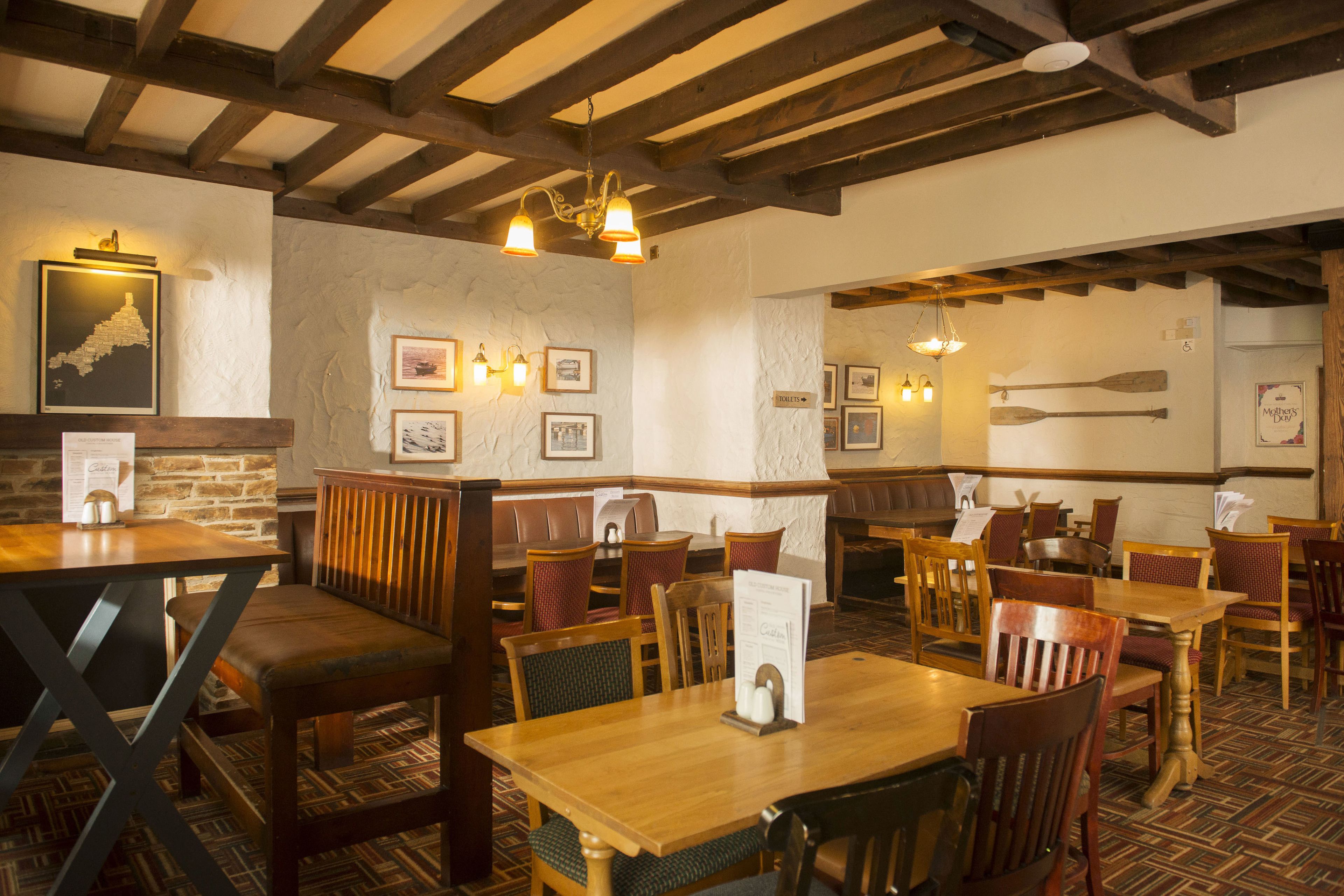 A restaurant interior with wooden tables and chairs, stone walls, and framed pictures on the walls.