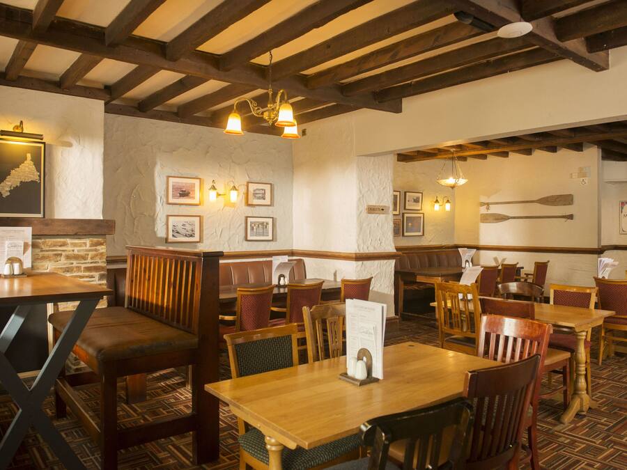 A restaurant interior with wooden tables and chairs, stone walls, and framed pictures on the walls.