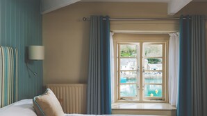 Habitación de hotel con cama, ventana con cortinas, vista a una piscina y una lámpara de pared.