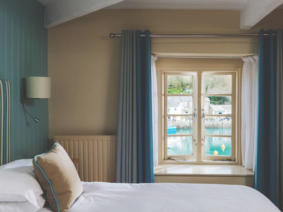 Habitación de hotel con cama, ventana con cortinas, vista a una piscina y una lámpara de pared.
