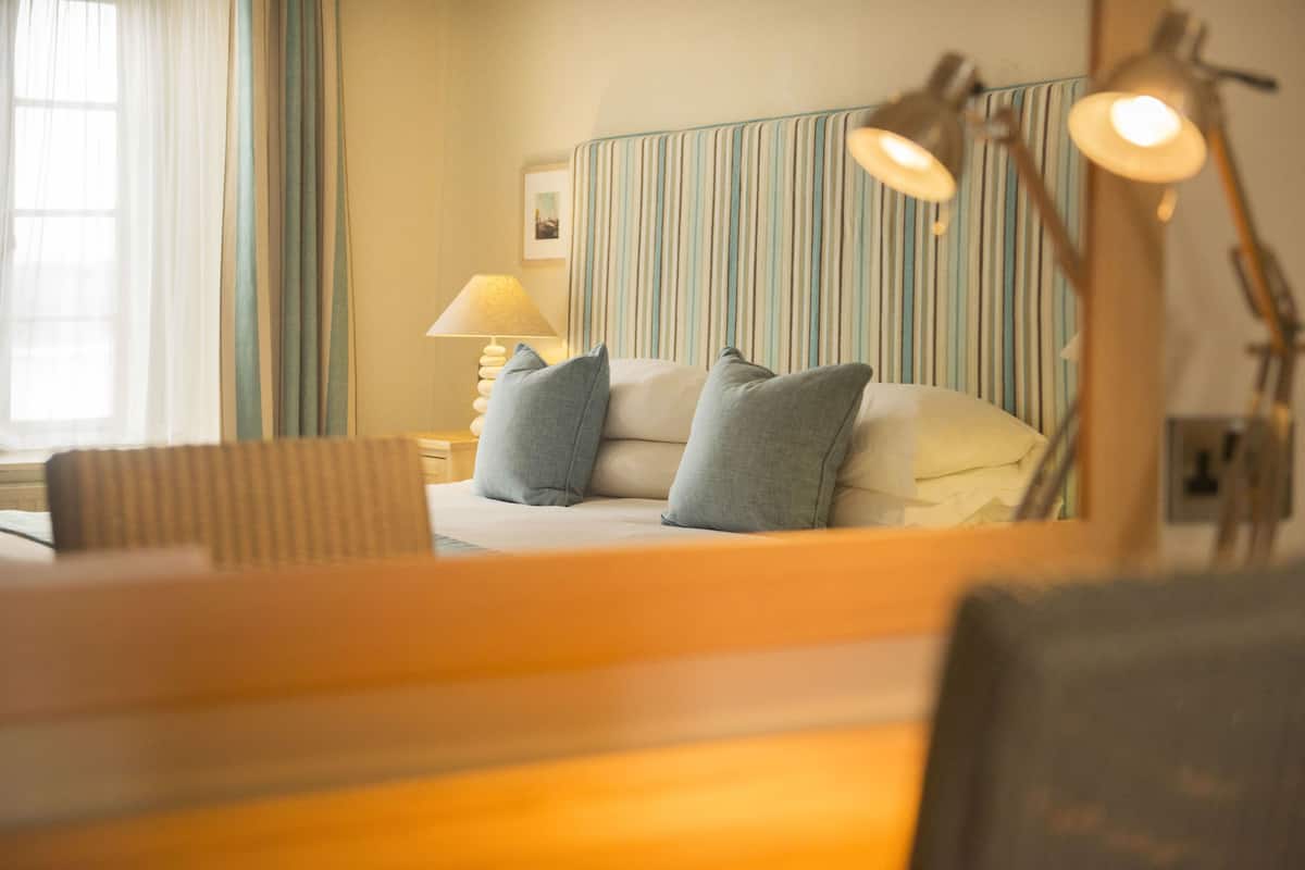 A hotel room with a bed, a bedside lamp, a chair, and a striped headboard.