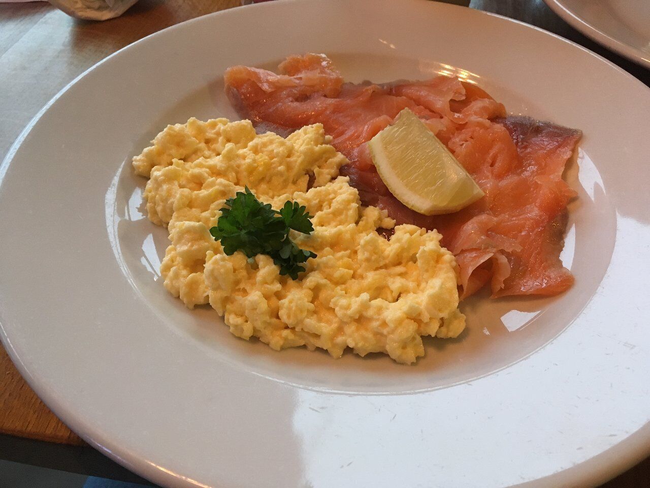 Une assiette avec des œufs brouillés, du saumon fumé et un quartier de citron.