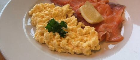 Une assiette avec des œufs brouillés, du saumon fumé et un quartier de citron.