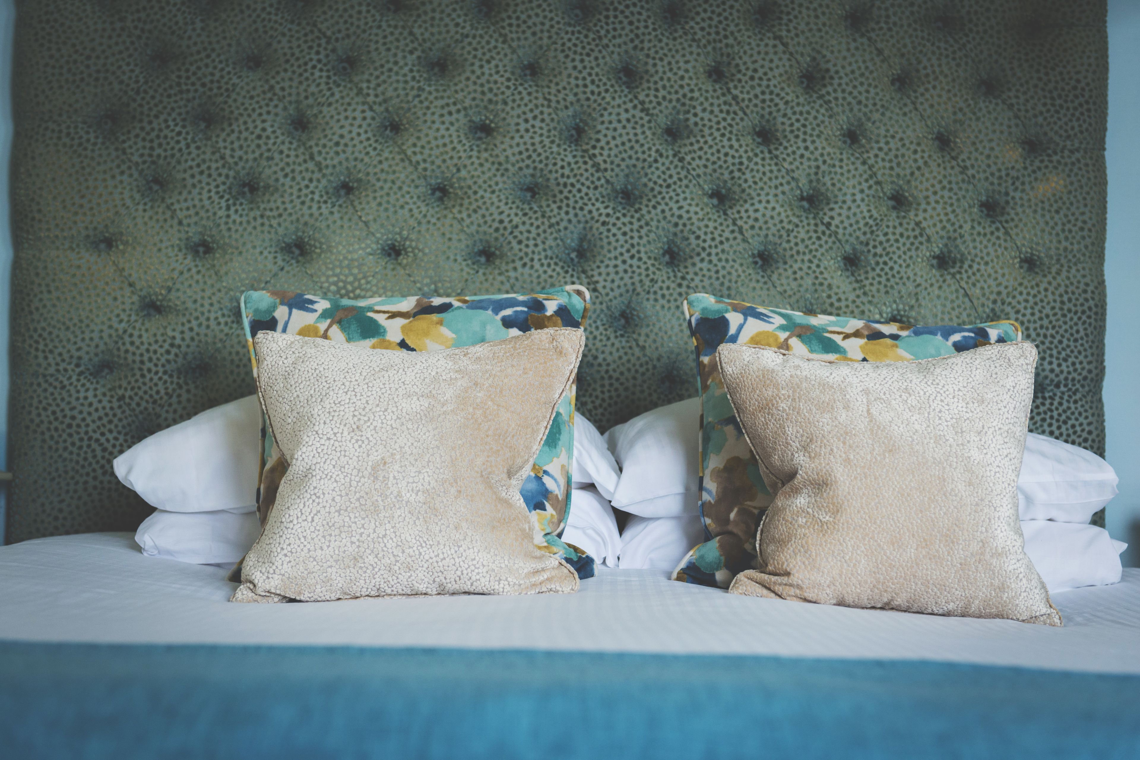 Una cama con dos almohadones decorativos, cabecera capitonada y ropa de cama blanca.
