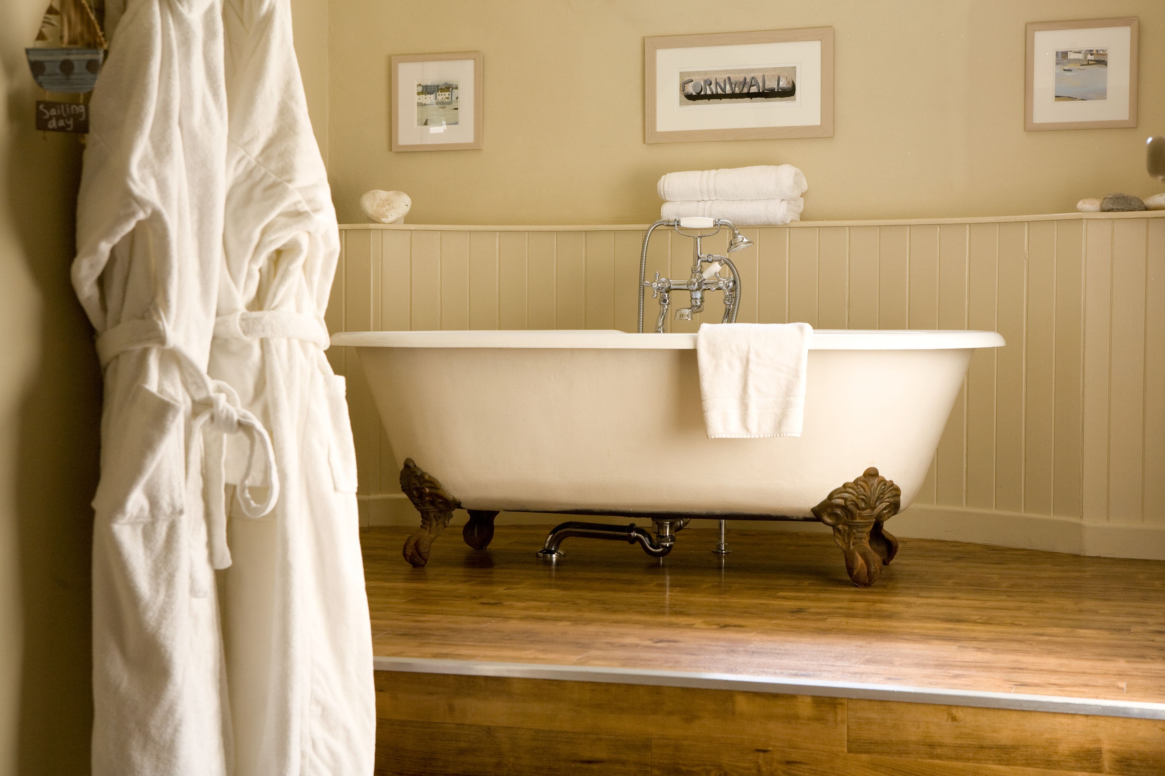 A bathroom with a freestanding bathtub, wooden flooring, and framed pictures on the wall.