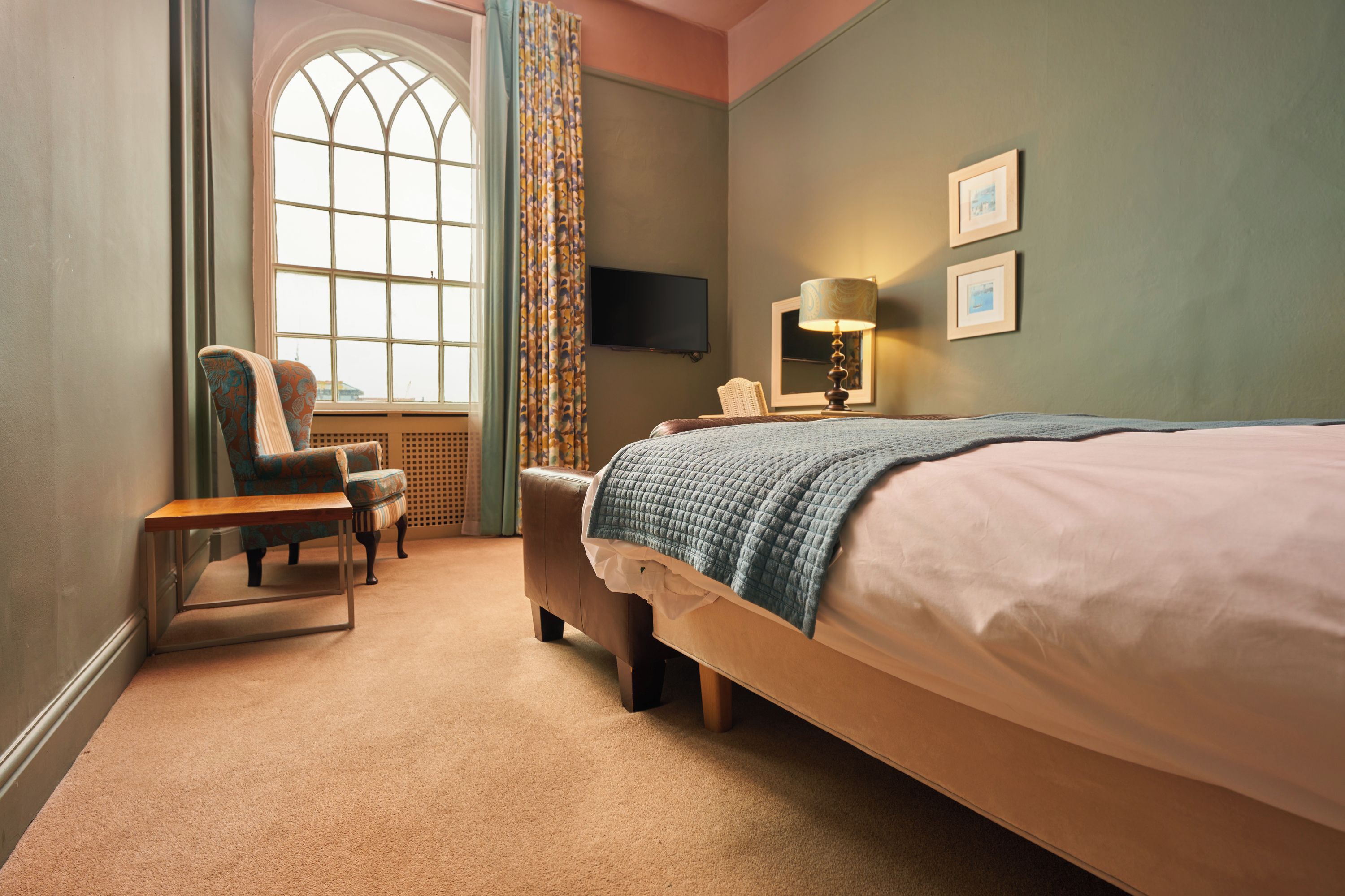 A hotel room with a large bed, a chair, a small table, a television, and a window with curtains.