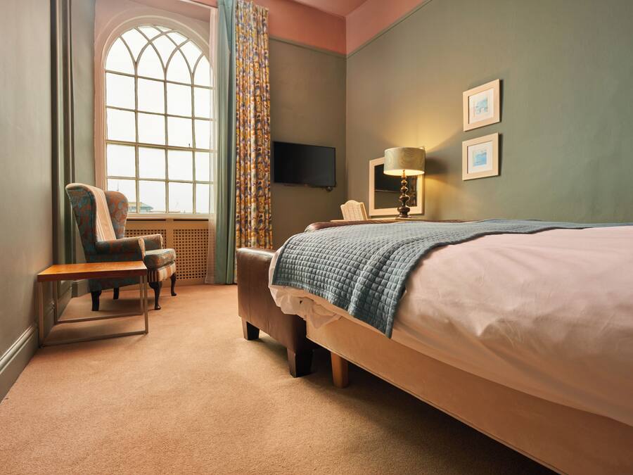 A hotel room with a large bed, a chair, a small table, a television, and a window with curtains.