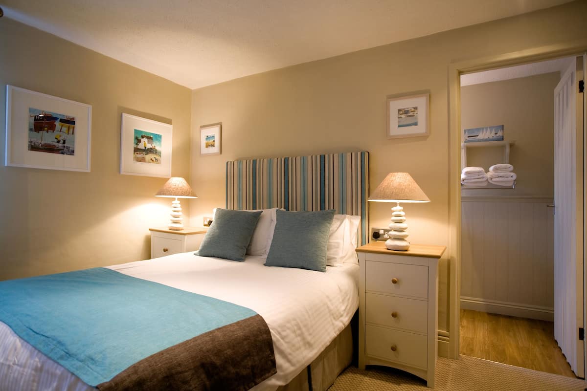A neatly arranged bedroom with a bed, bedside tables with lamps, a wardrobe, and framed pictures on the wall.