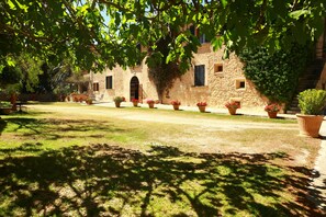A courtyard with a stone building, potted plants, and a clear sky. - Hotel Agroturismo Possessió Binicomprat (Algaida)