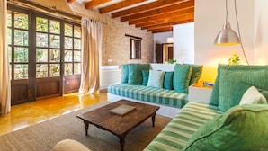 Una sala de estar acogedora con techo de madera, un sofá verde a rayas, una mesa de centro de madera y un ventanal con cortinas.
