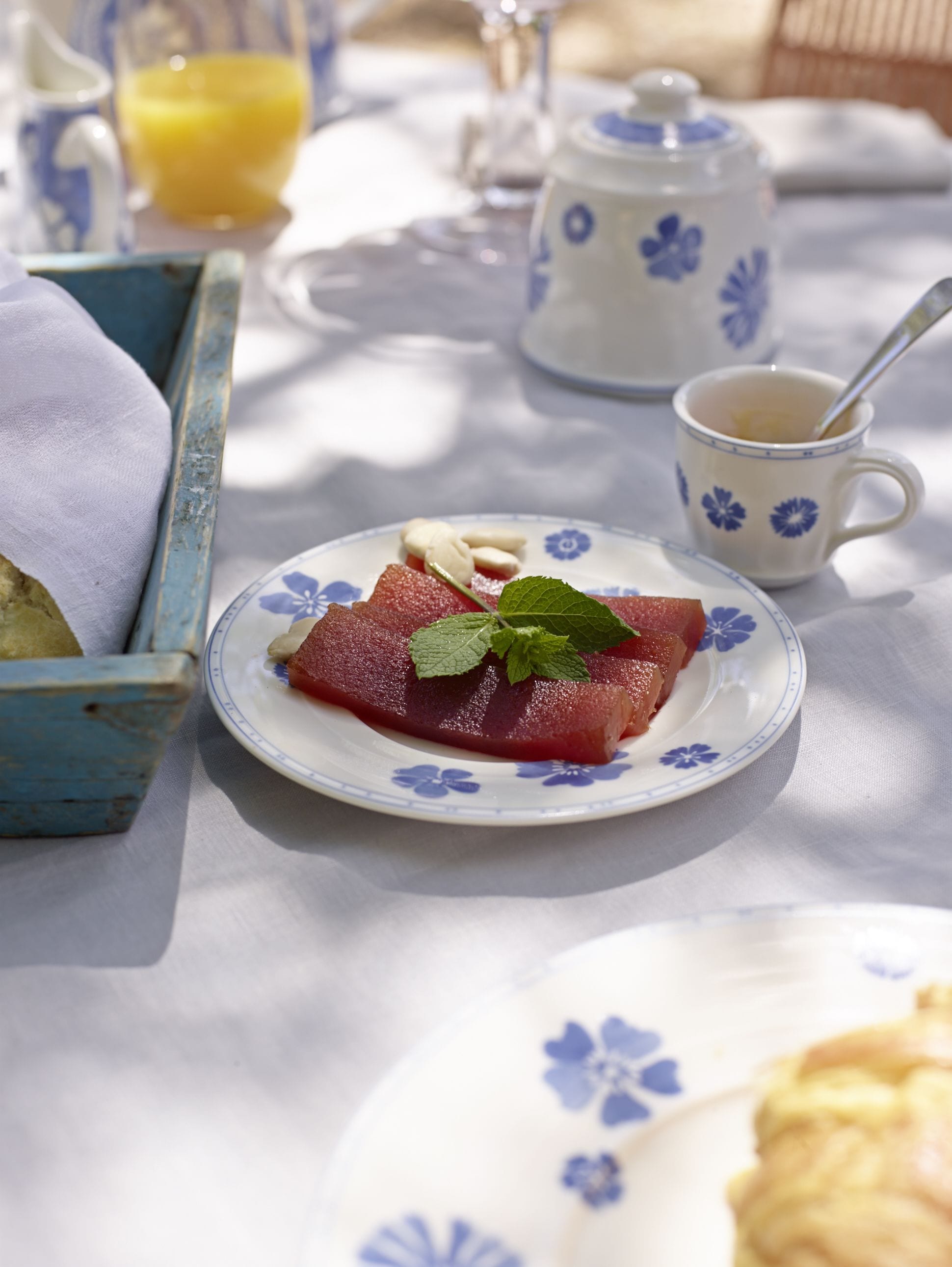 A breakfast setting with a plate of sliced fruit, a cup of coffee, and a jug of orange juice on a table.