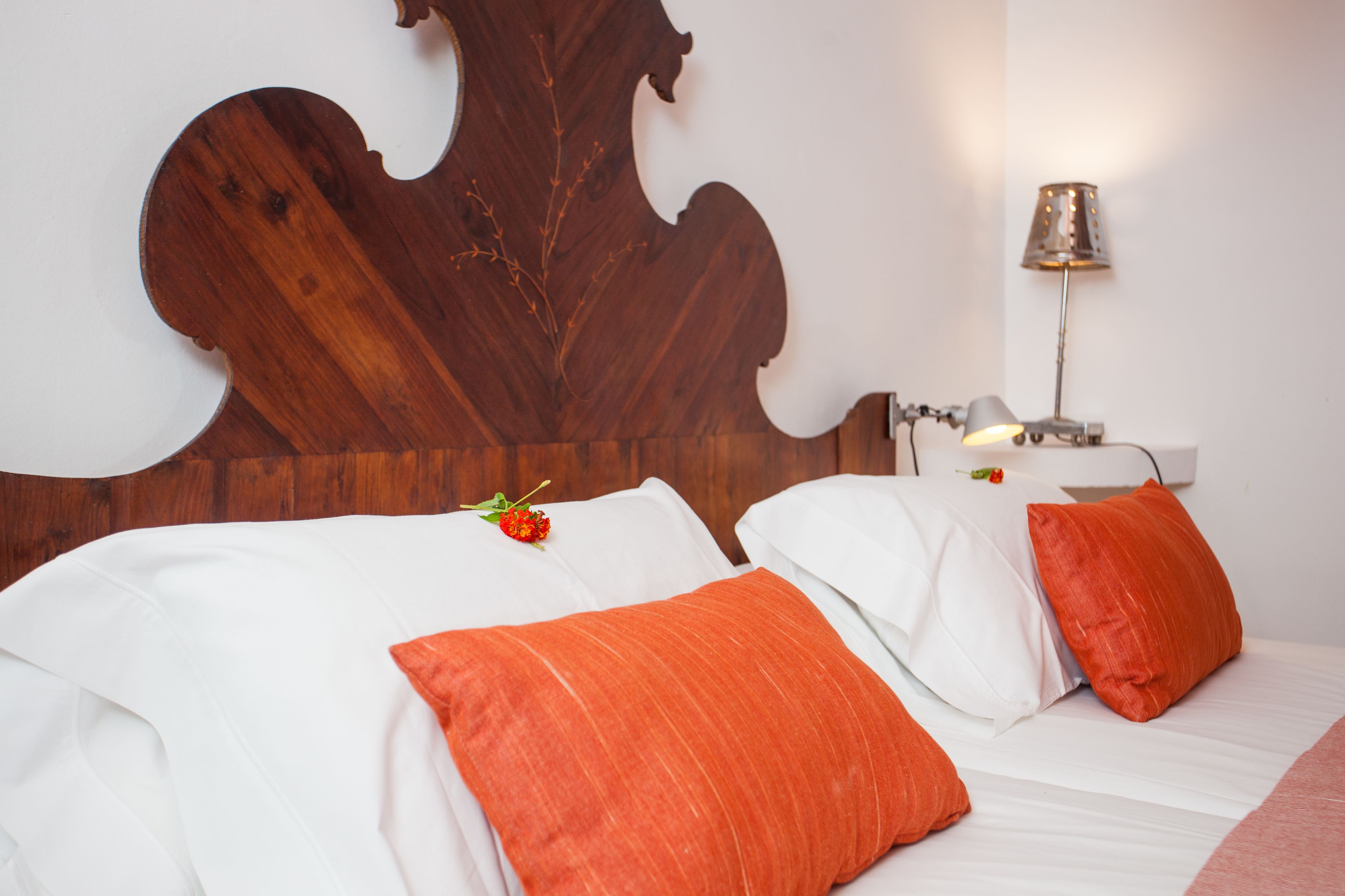 A hotel room with a large wooden headboard, white bedding, and a single bedside table with a lamp.