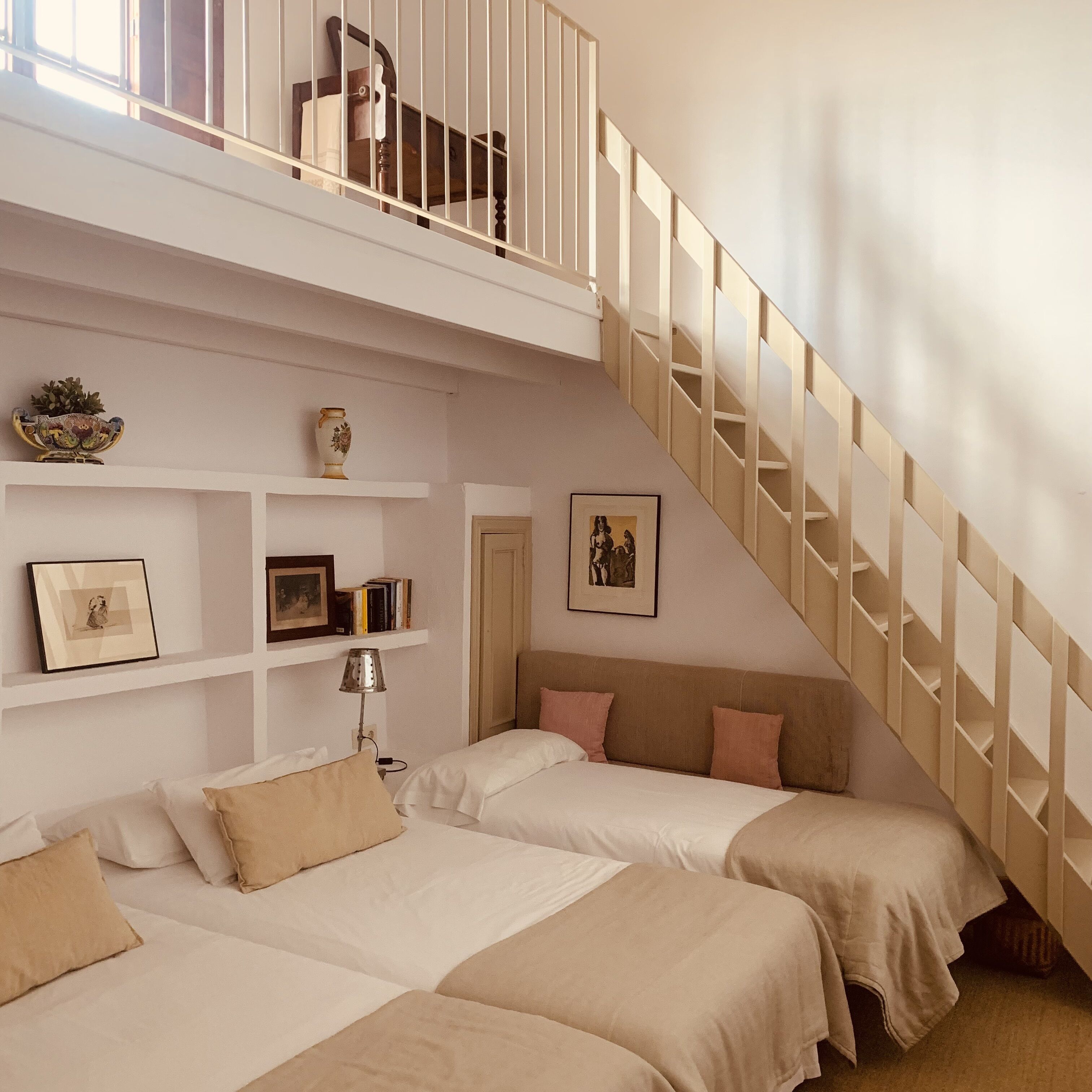 Une chambre avec deux lits, un escalier et une étagère ornée d’objets décoratifs.