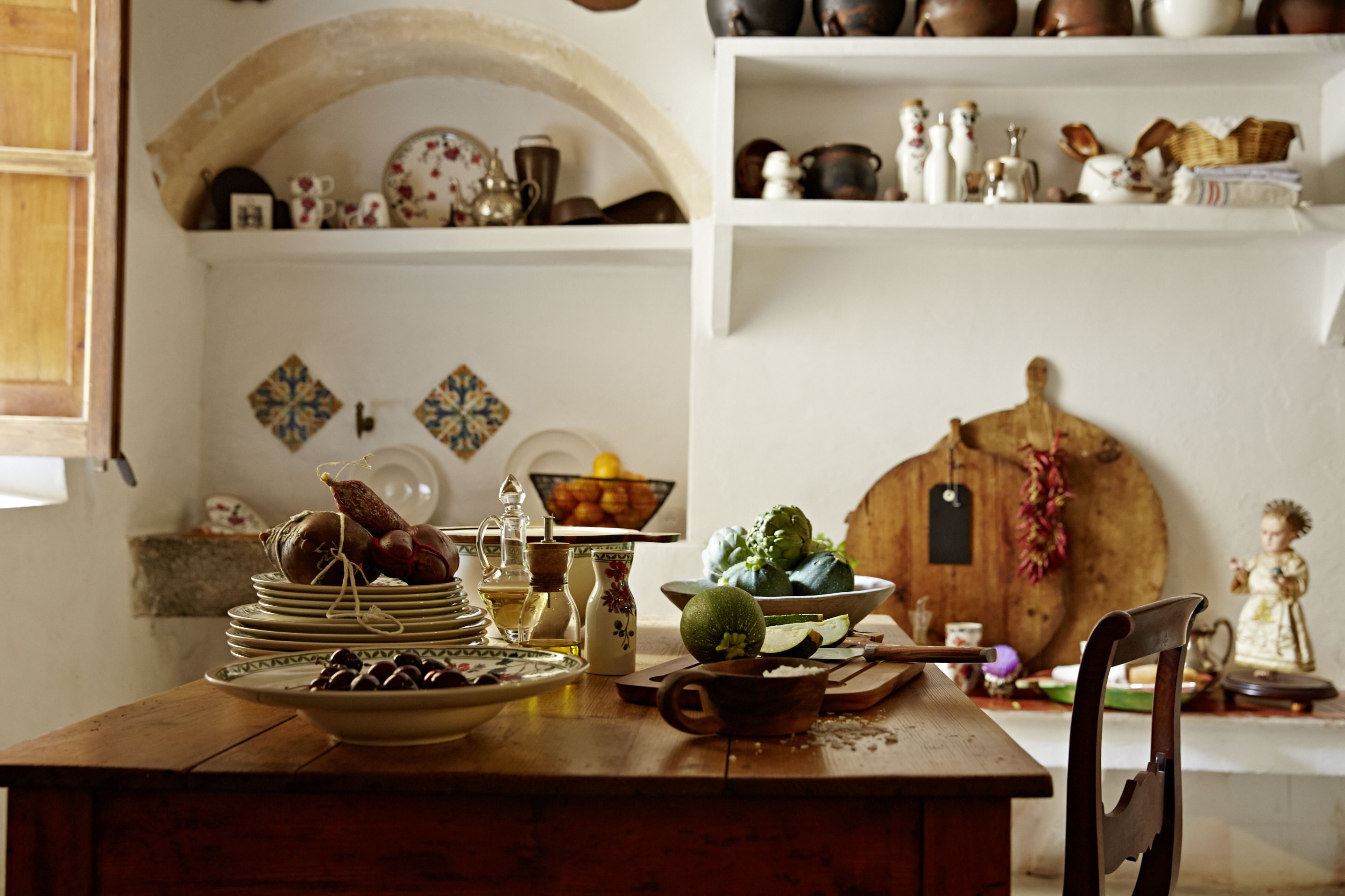 Una cocina rústica con una mesa de madera, estantes con utensilios de cocina y un adorno de madera.