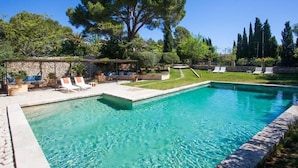 Una piscina rectangular de aguas cristalinas y color azul, rodeada por un muro de piedra y una zona verde con sillas de descanso.
