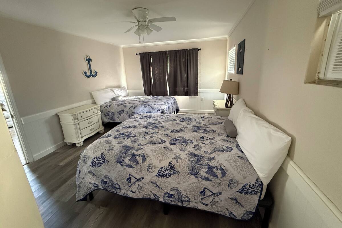 A bedroom with two beds, a ceiling fan, a window with curtains, a nightstand, and a dresser.