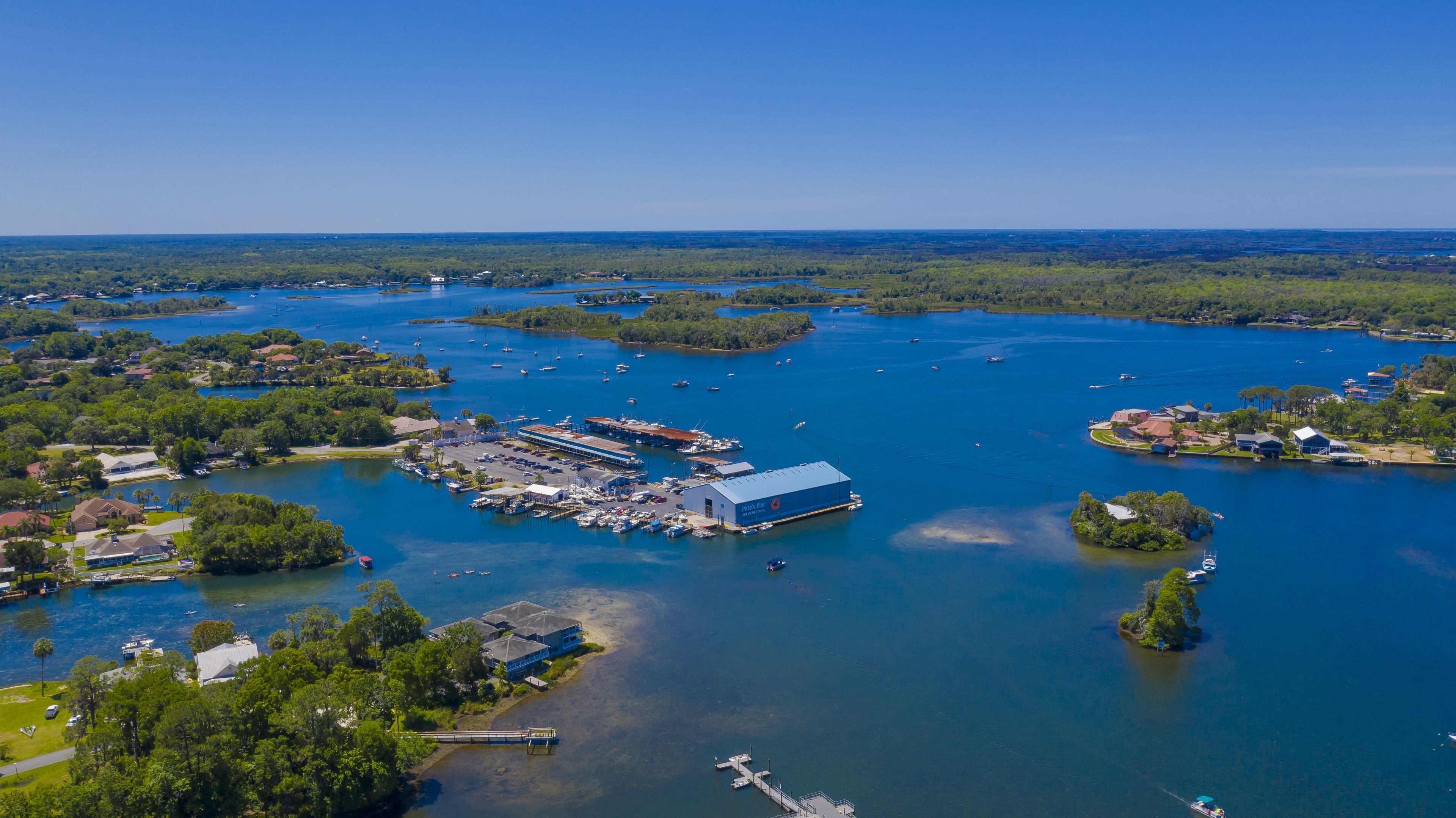 En vy från ovan över en småbåtshamn med båtar, en stor byggnad med skylten ”Pier’s Point Marina” och omgivande grönska.
