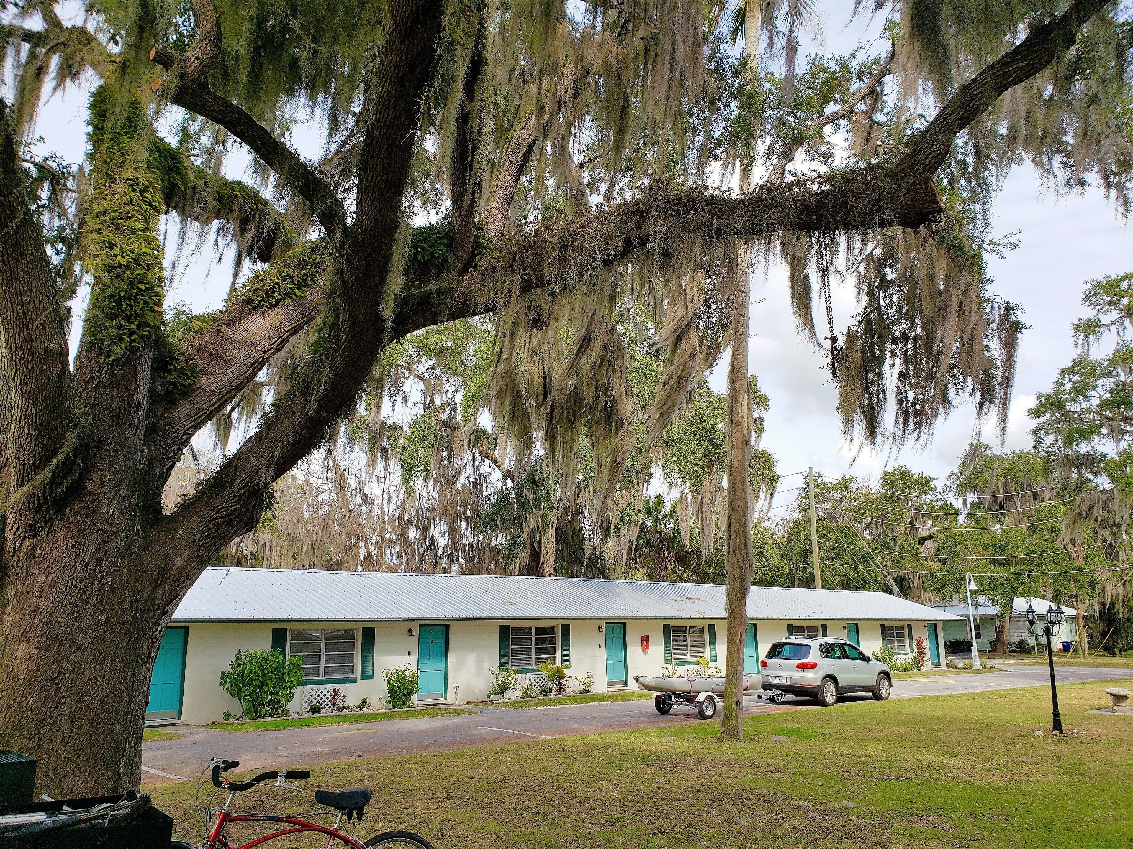 A motel with a white exterior and green trim, a parked bicycle, and a car in the driveway.