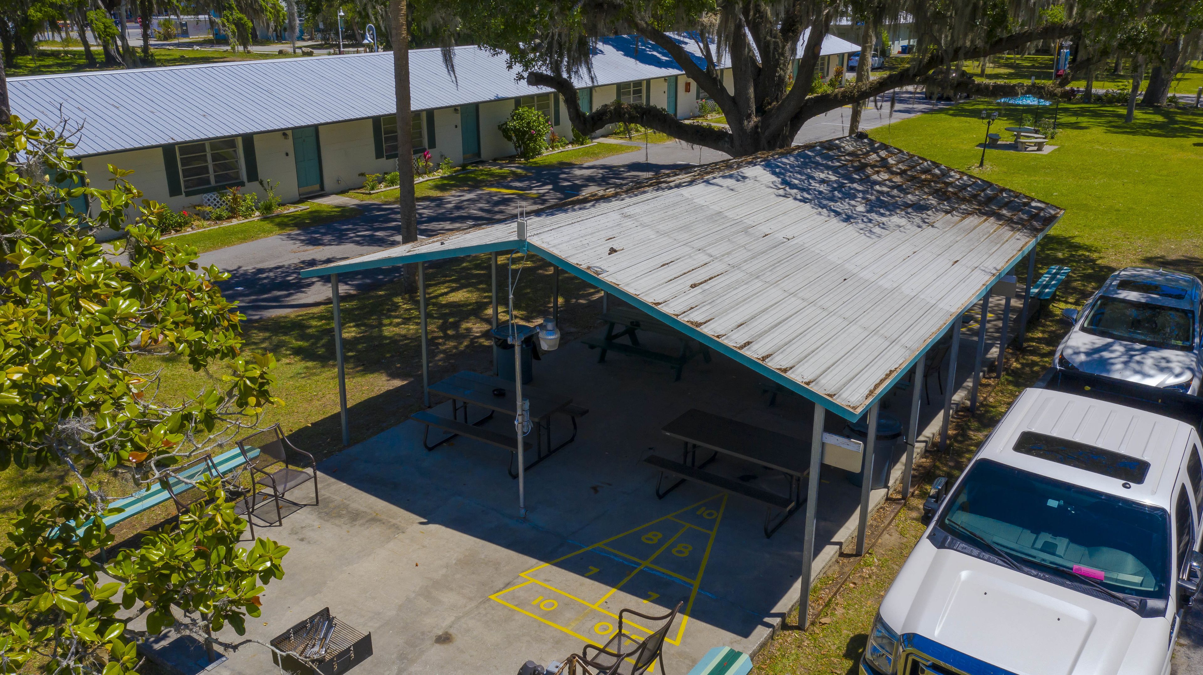 An outdoor covered parking area with picnic tables and benches, adjacent to a building with a metal roof.